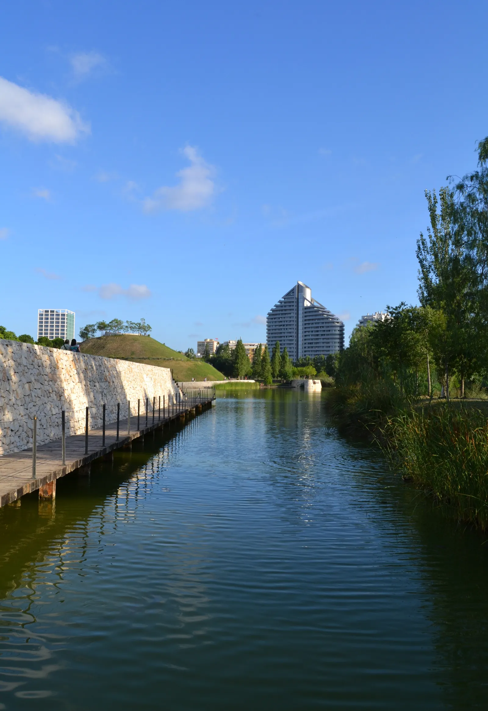 Wasserlauf im Parc de Capcalera mit Rasenufern und Bäumen auf beiden Seiten.
