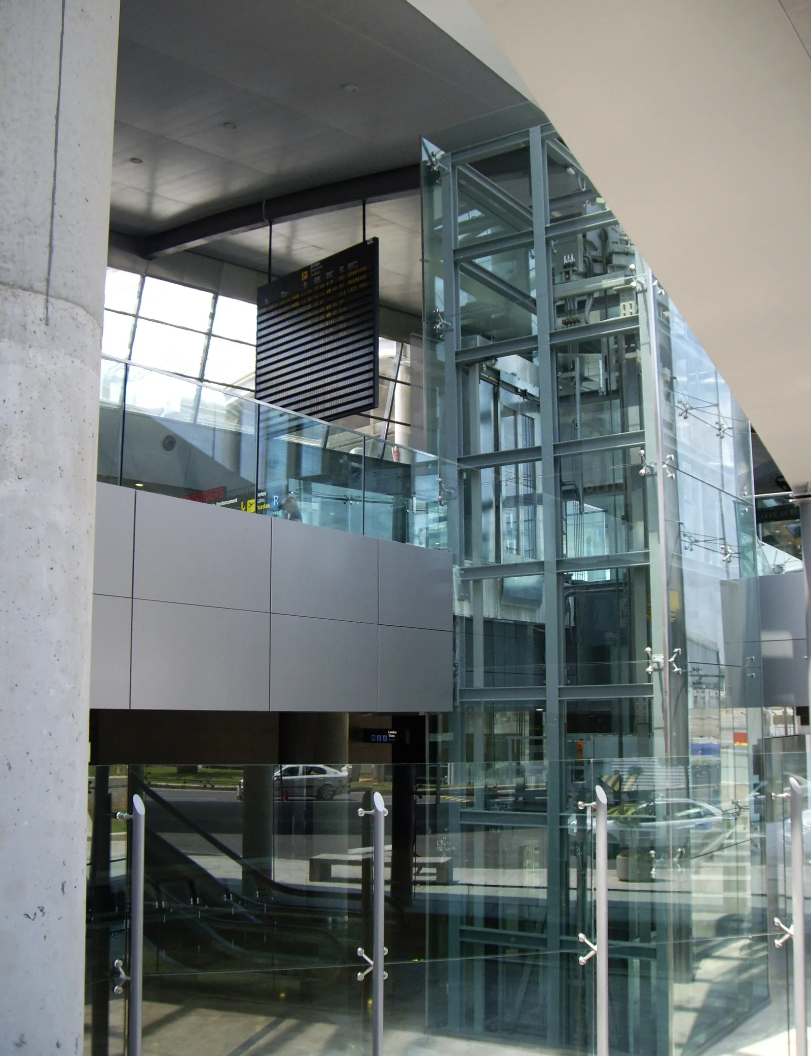 Gläserner Aufzug und Rolltreppen im Terminalgebäude eines Flughafens