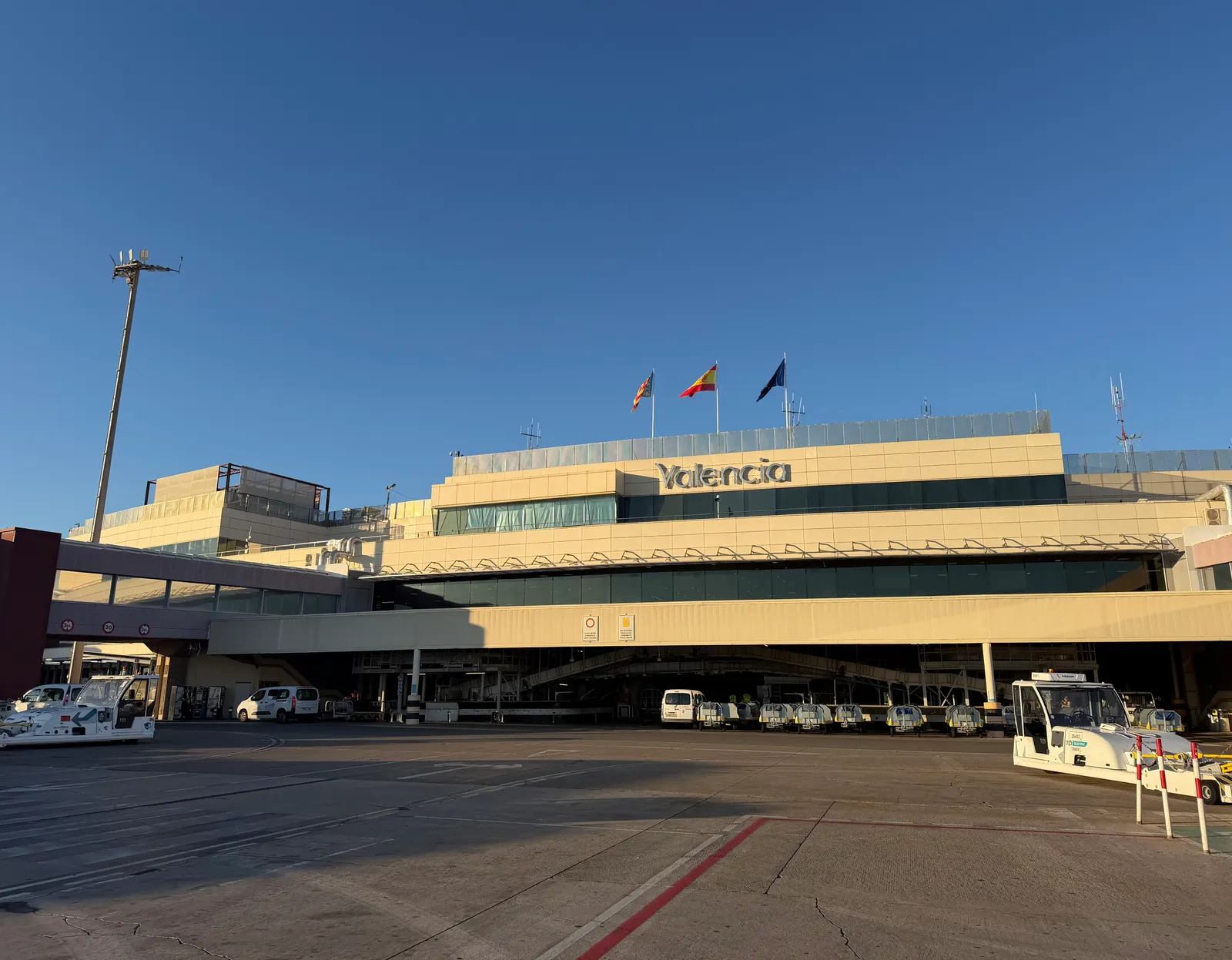 Vorderseite des Terminalgebäudes des Flughafens Valencia mit dem Flughafennamen auf dem Dach und Servicefahrzeugen davor