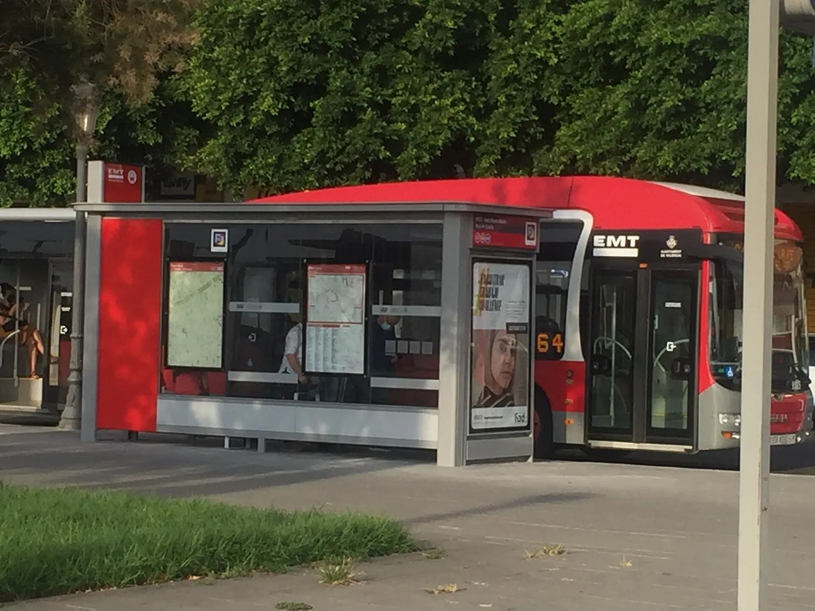 Roter Stadtbus neben einer überdachten Haltestelle mit Fahrplantafel und Bäumen dahinter