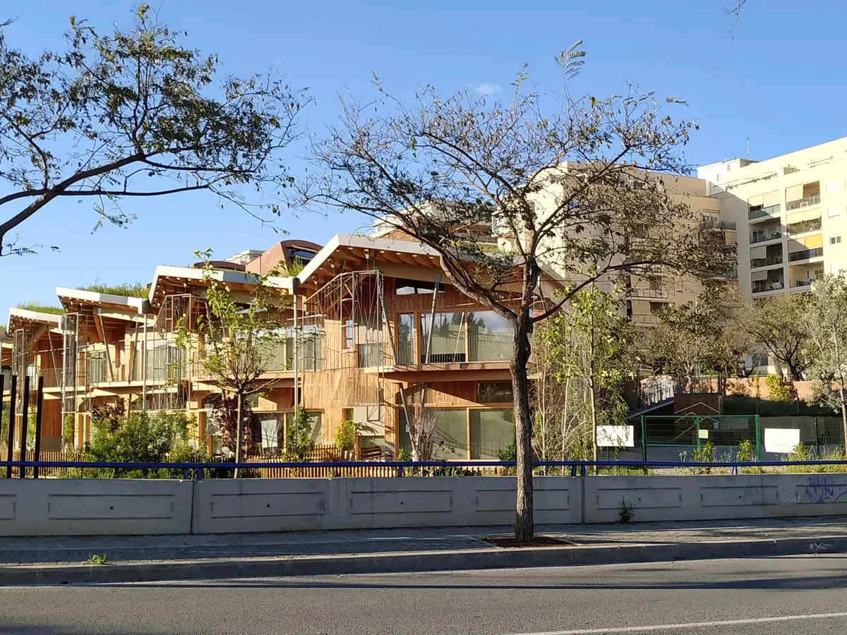 Schulgebäude aus Holz und Backstein mit Terrassen hinter Bäumen, von der Straße gesehen