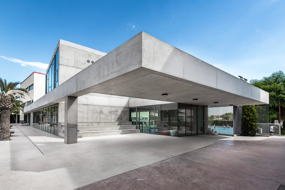 Betongebäude einer Schule mit breitem Flachdach und Glaswänden neben einem Sportplatz