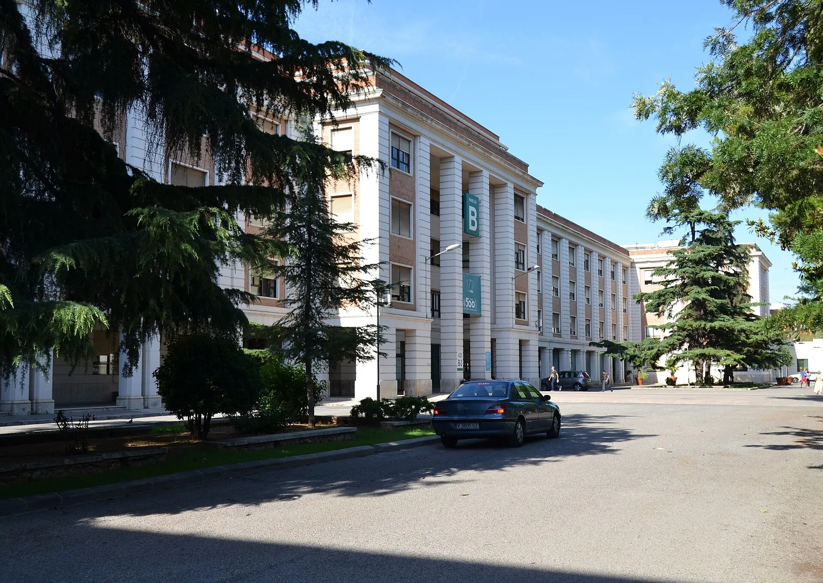 Krankenhausgebäude mit Säulenfassade, gesehen von einer ruhigen Straße mit Bäumen