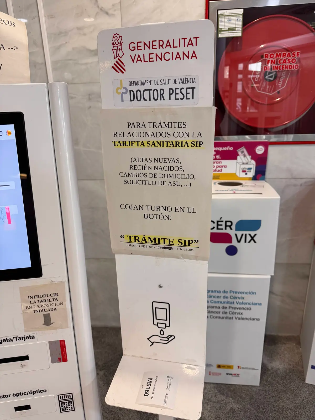 Hinweis neben einem Check-in-Automaten in einem Centro de salud, der SIP-Kartenanträge auf eine Taste am Bildschirm verweist