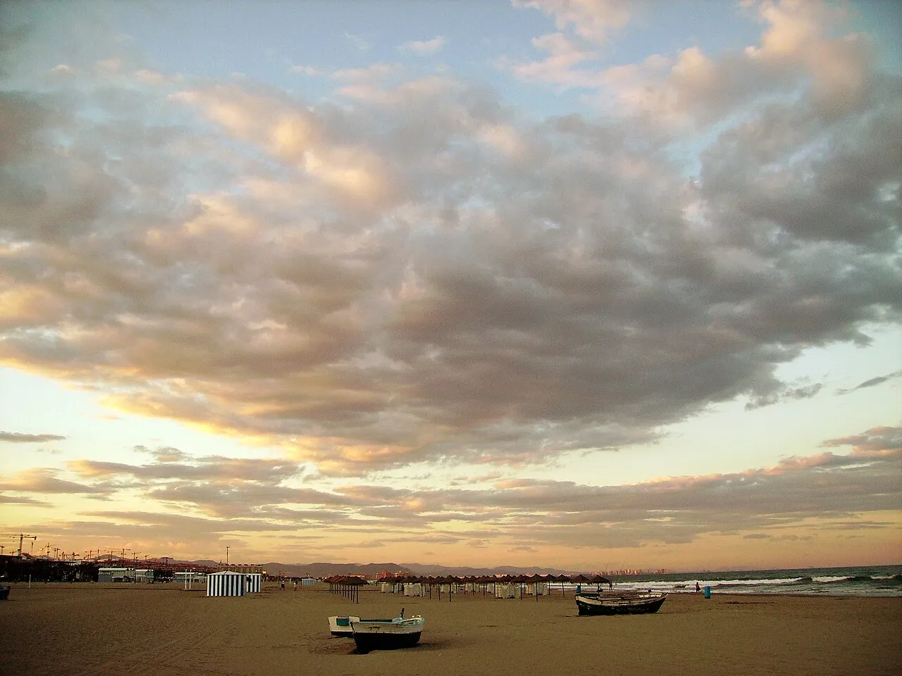 Sunset sky over the sand of Malvarrosa beach with two boats on the shore.