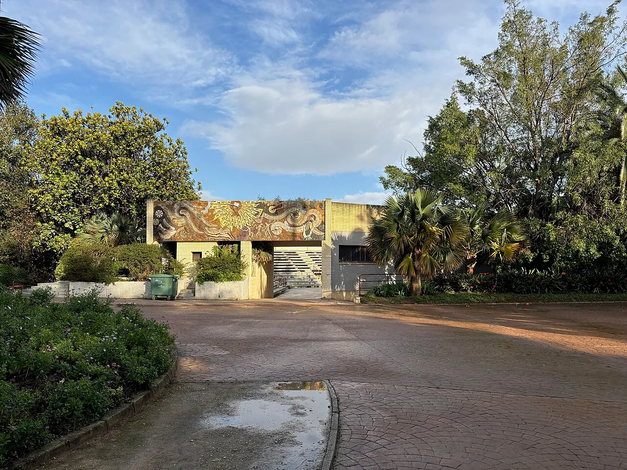 Tree-lined path and a low building at the entrance of the Parque de Benicalap.