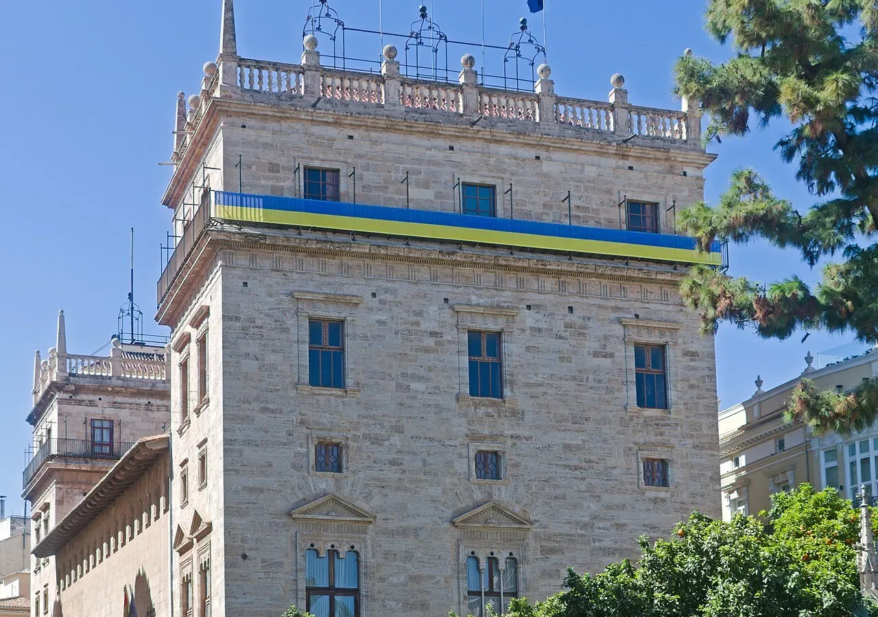 Historischer Palast mit Steinturm und Reihen von Bogenfenstern unter blauem Himmel.